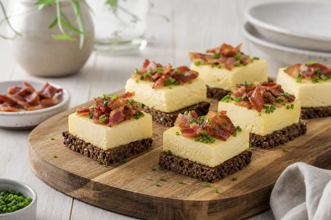 Æggestand skåret i tern på rugbrød med purløg og sprød bacon på et træbræt