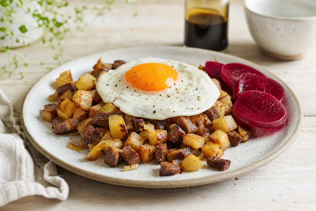 Sprød biksemad af kødtern, kartofler og løg med spejlæg ovenpå, serveret med rødbeder og worcestershiresauce