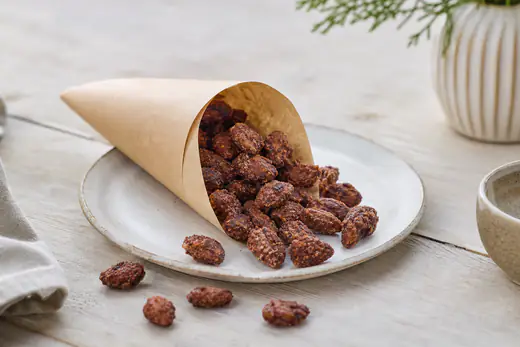 Brændte mandler med sprød, brun kanelsukkerskal i en lille papirkræmmerhus og på et bord