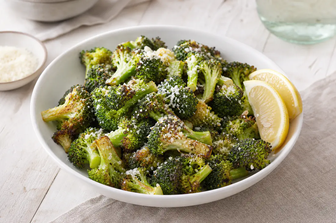 Ristede broccolibuketter med sprøde brune kanter, revet parmesan og citronbåde i en hvid skål