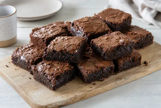 Firkantede brownies med blank, sprukken top og klistret midte på et skærebræt