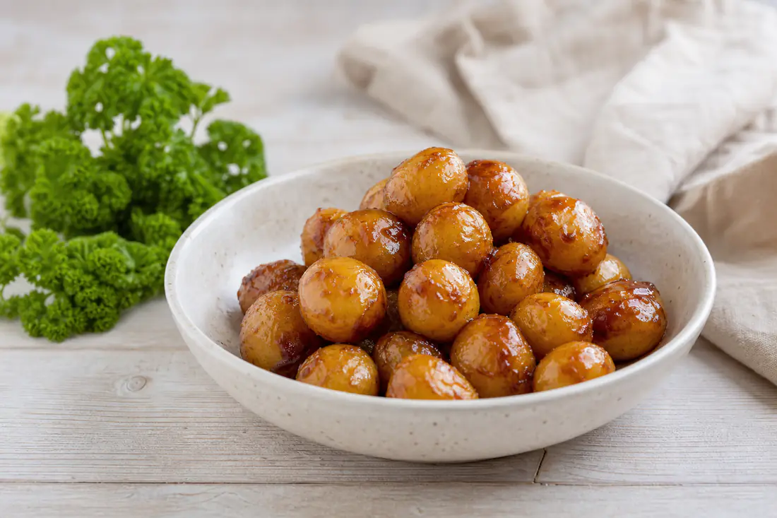 Små blanke brunede kartofler med gylden karamel i en skål med persille ved siden af