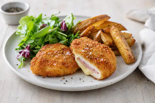 To gyldne cordon bleu skåret over, så smeltet ost og skinke kan ses, med kartofler og salat