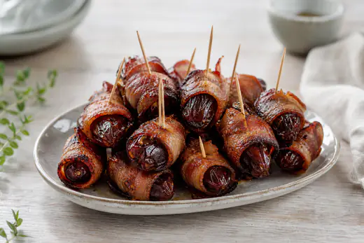 Dadler viklet ind i sprød bacon serveret på et lille fad med tandstikker