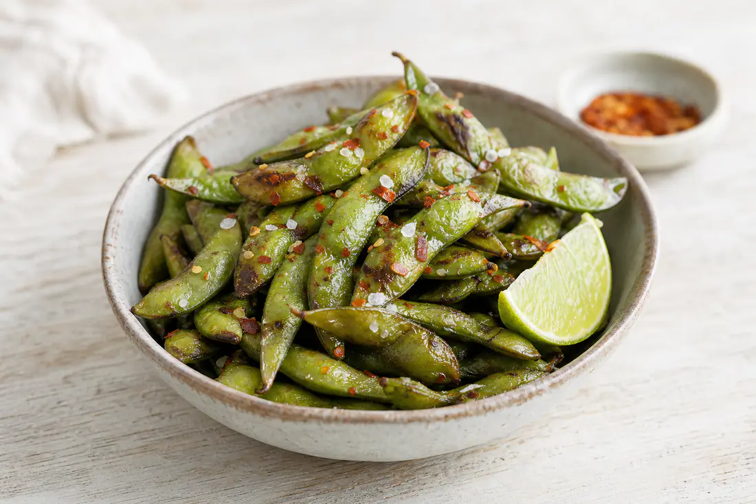 Ristede edamamebælg med flagesalt og chiliflager i en lille skål med limebåd