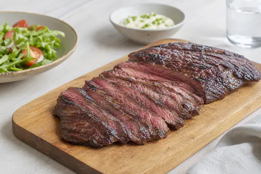 Rosa flanksteak skåret i tynde skiver på tværs af fibrene på et skærebræt