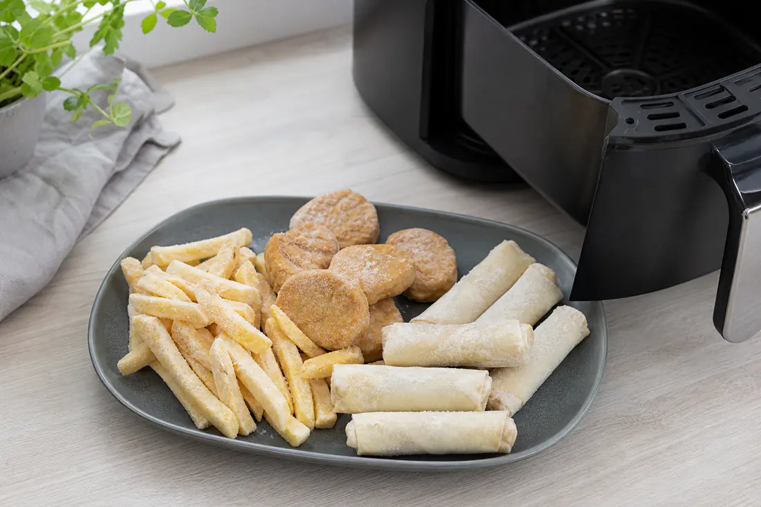 Frosne pommes frites, nuggets og forårsruller med rimfrost på en bakke ved siden af en airfryerkurv