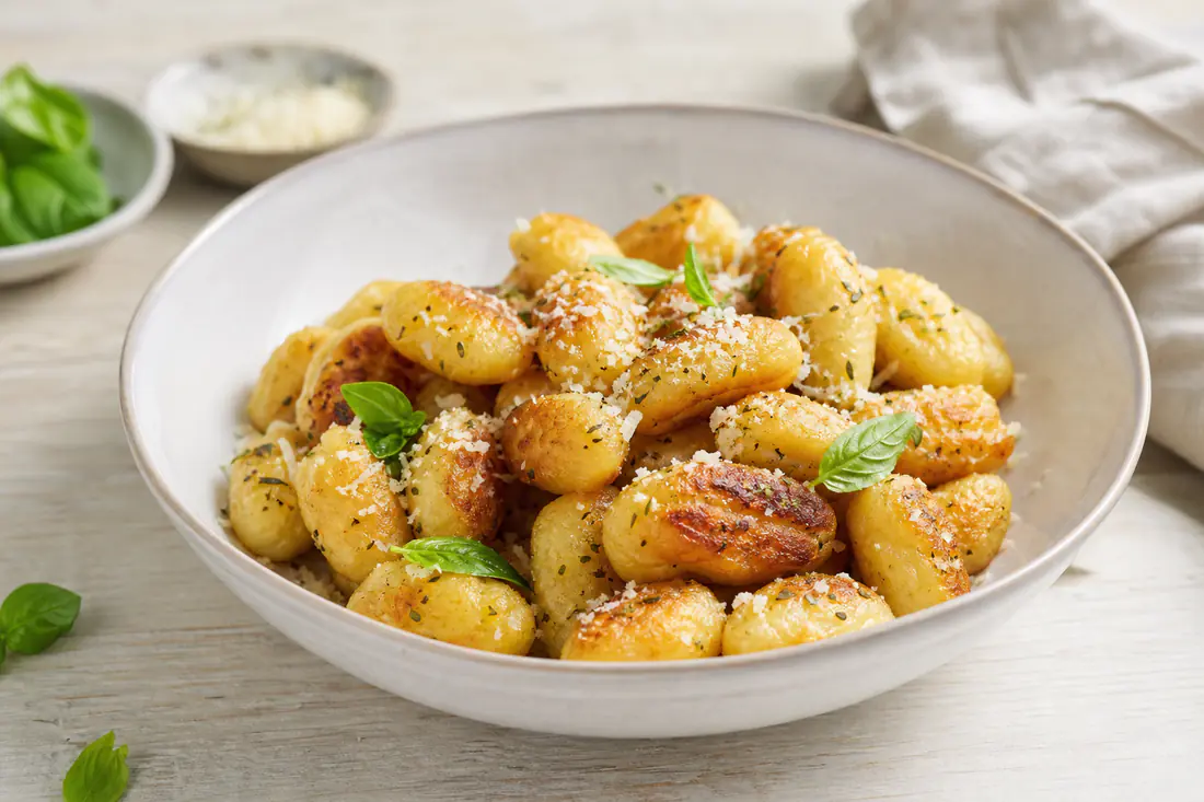 Gyldne sprøde gnocchi med revet parmesan, oregano og friske basilikumblade i en lav skål