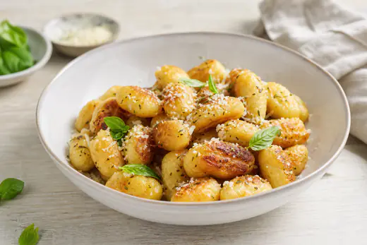Gyldne sprøde gnocchi med revet parmesan, oregano og friske basilikumblade i en lav skål
