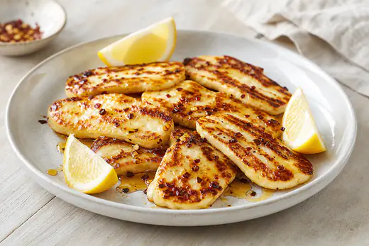 Gyldenbrune halloumiskiver med honning, chiliflager og citronbåde på en tallerken