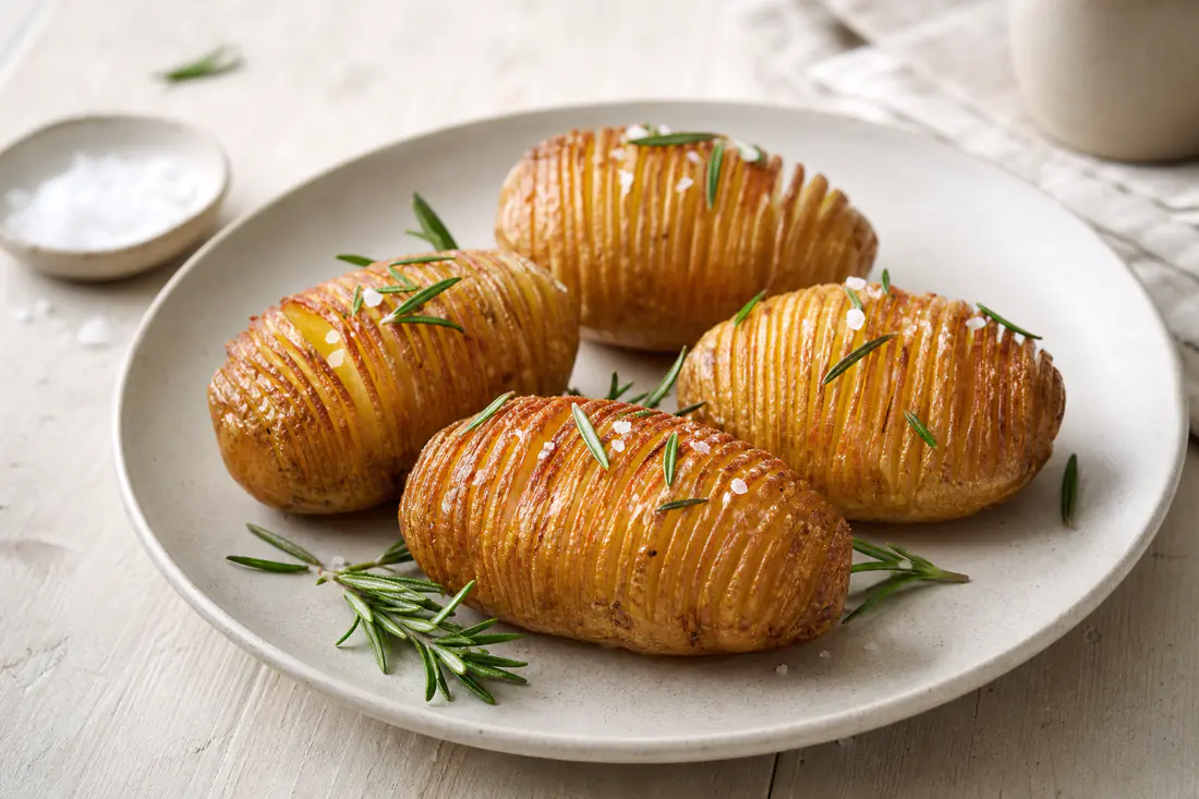 Fire hasselbagte kartofler med gyldne, sprøde lameller, flagesalt og rosmarin på en tallerken