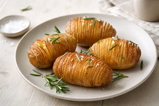 Fire hasselbagte kartofler med gyldne, sprøde lameller, flagesalt og rosmarin på en tallerken