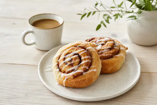 Gyldne kanelsnegle med hvid glasur på et fad, hvor spiralen af kanel og sukker tydeligt kan ses