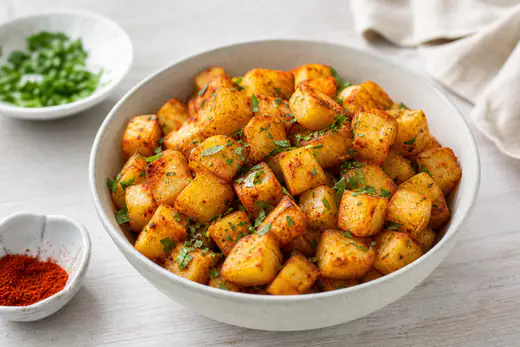 Gyldne sprøde kartoffeltern med paprika og hakket persille i en lys keramikskål