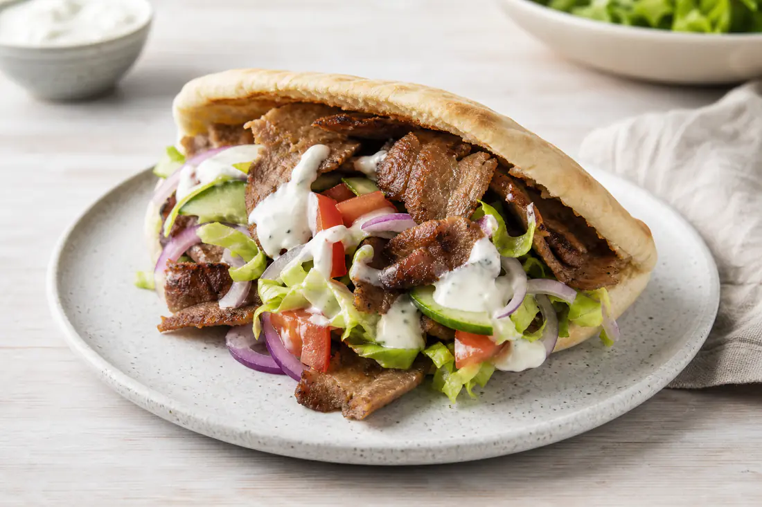 Pitabrød fyldt med varmt kebabkød, salat, agurk, tomat, rødløg og hvidløgsdressing på en tallerken