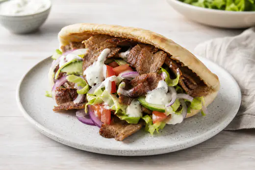 Pitabrød fyldt med varmt kebabkød, salat, agurk, tomat, rødløg og hvidløgsdressing på en tallerken