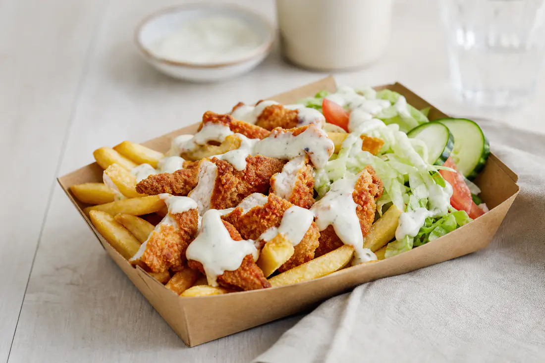 Kyllingemix i en papbakke med pommes frites, sprøde kyllingestykker, salat, agurk, tomat og hvid dressing