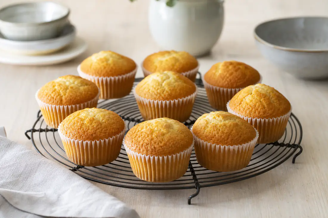 Gyldne vaniljemuffins med hvælvet top i papirforme på en bagerist