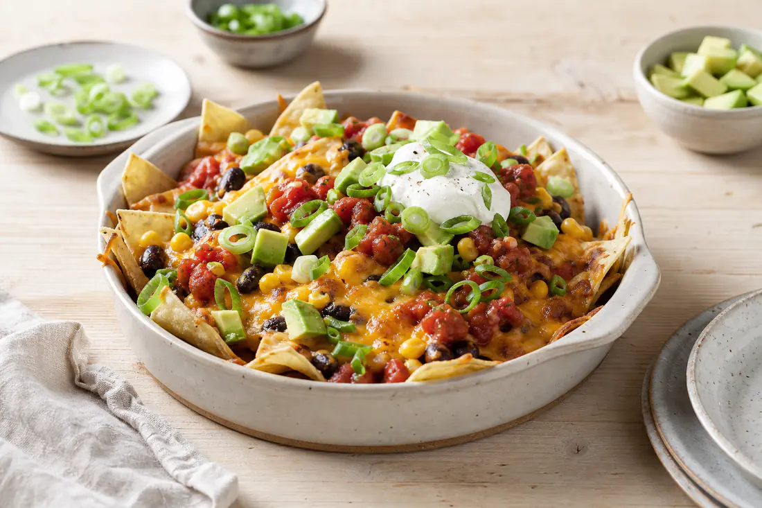 Ostebagte nachos med sorte bønner, majs, salsa, avocado, creme fraiche og forårsløg i en lille form