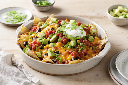 Ostebagte nachos med sorte bønner, majs, salsa, avocado, creme fraiche og forårsløg i en lille form