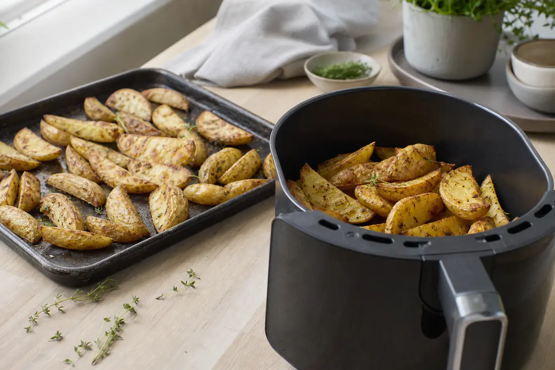 Bageplade med kartoffelbåde fra ovnen ved siden af en airfryerkurv med samme ret