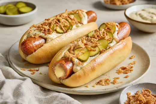Gyldne ostepølser i hotdogbrød med remoulade, ristede løg og agurkesalat, hvor smeltet ost ses i pølsen
