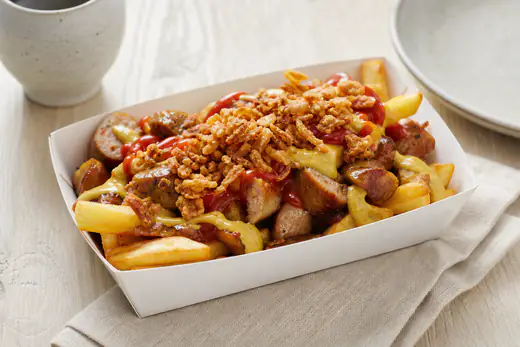 Pølsemix i en papbakke med sprøde pommes frites og brunede pølsestykker toppet med ketchup, remoulade og ristede løg