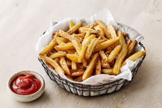 Gyldne hjemmelavede pommes frites med flagesalt i en papirforet kurv med en lille skål ketchup ved siden af