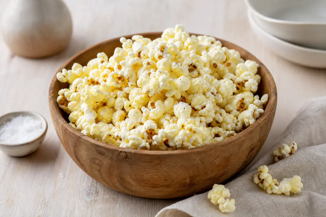 Lune popcorn med smør og flagesalt i en træskål på et lyst bord