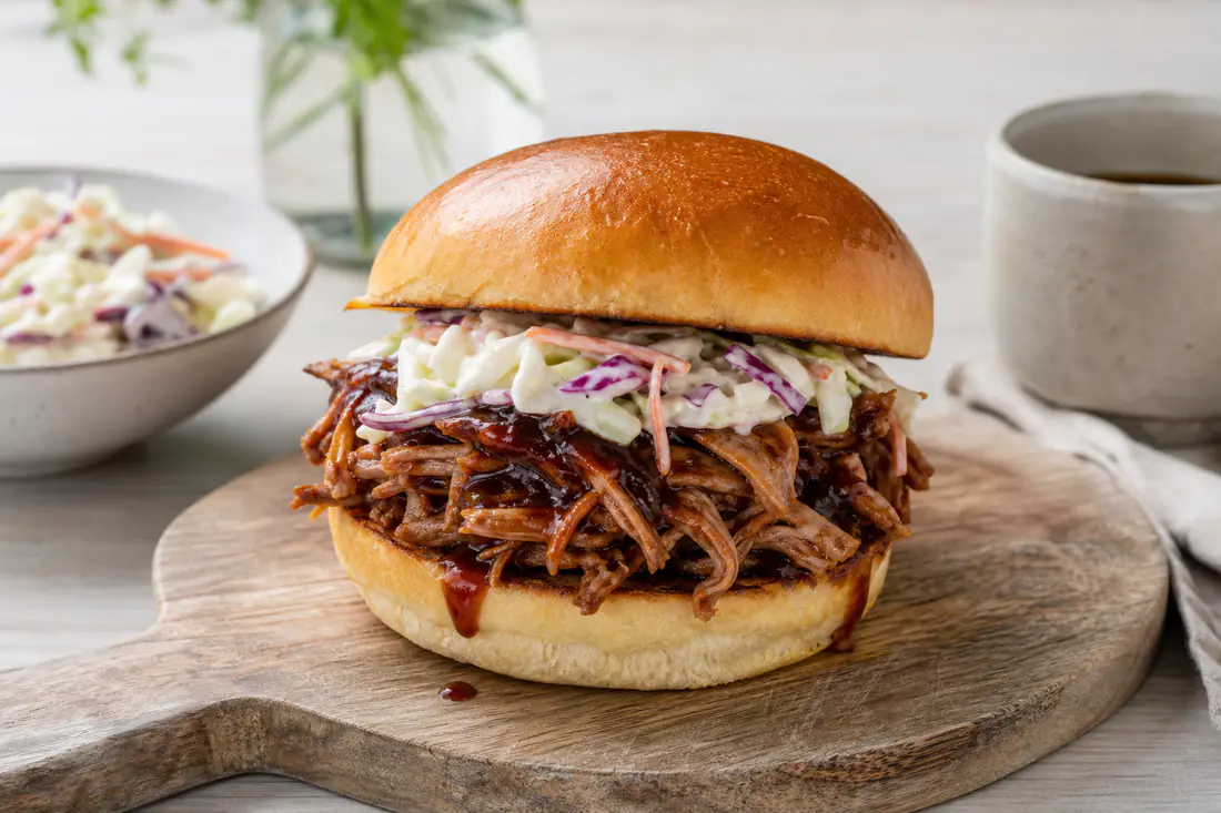 Trævlet pulled pork med BBQ-sauce i en briochebolle med coleslaw på et træbræt