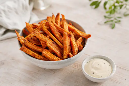 Gyldne stave af søde kartofler med paprika i en lille skål med dip ved siden af