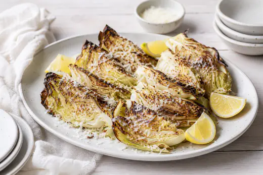 Ristede både af spidskål med brune kanter, revet parmesan og citronbåde på et serveringsfad