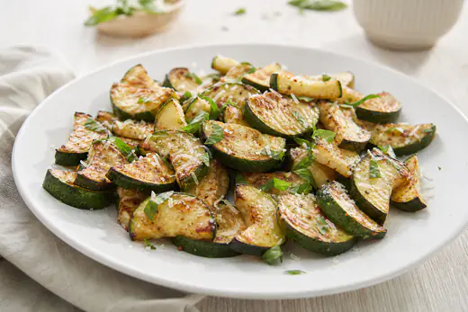 Gyldenbrune halvmåner af squash drysset med parmesan og frisk basilikum på en hvid tallerken