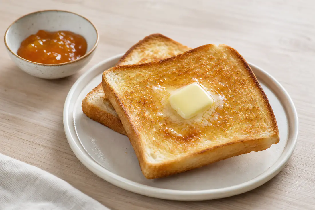 Gyldne skiver ristet toastbrød med smeltende smør og en lille skål marmelade på en tallerken