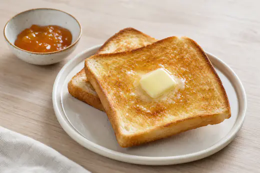 Gyldne skiver ristet toastbrød med smeltende smør og en lille skål marmelade på en tallerken