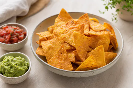 Gyldne, hjemmelavede tortillachips i trekanter i en skål med salsa og guacamole ved siden af