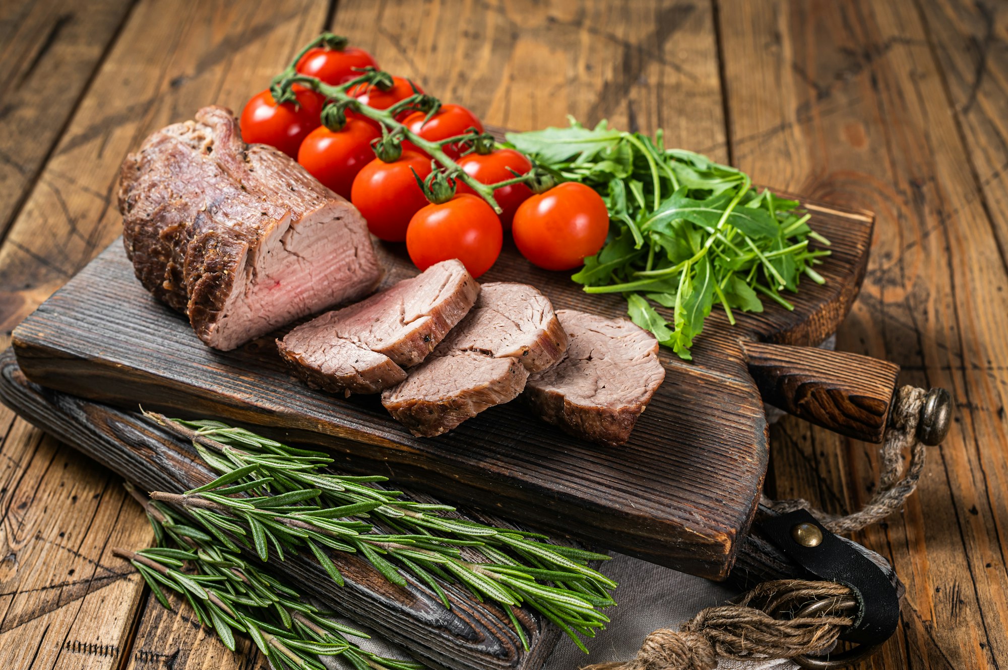 Roast Veal tenderloin, sliced Roastbeef on wooden board with garnish. Wooden background. Top view