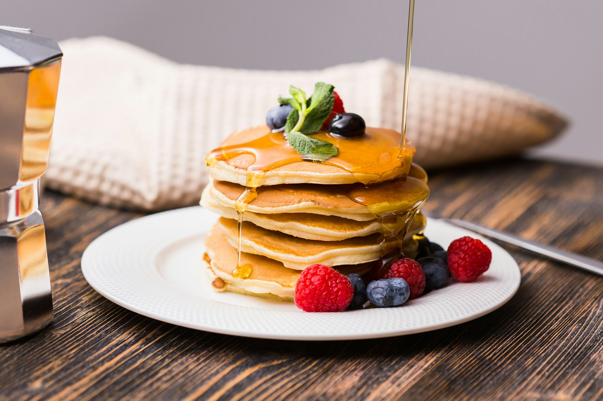 Woman pouring maple syrup on tasty pancakes