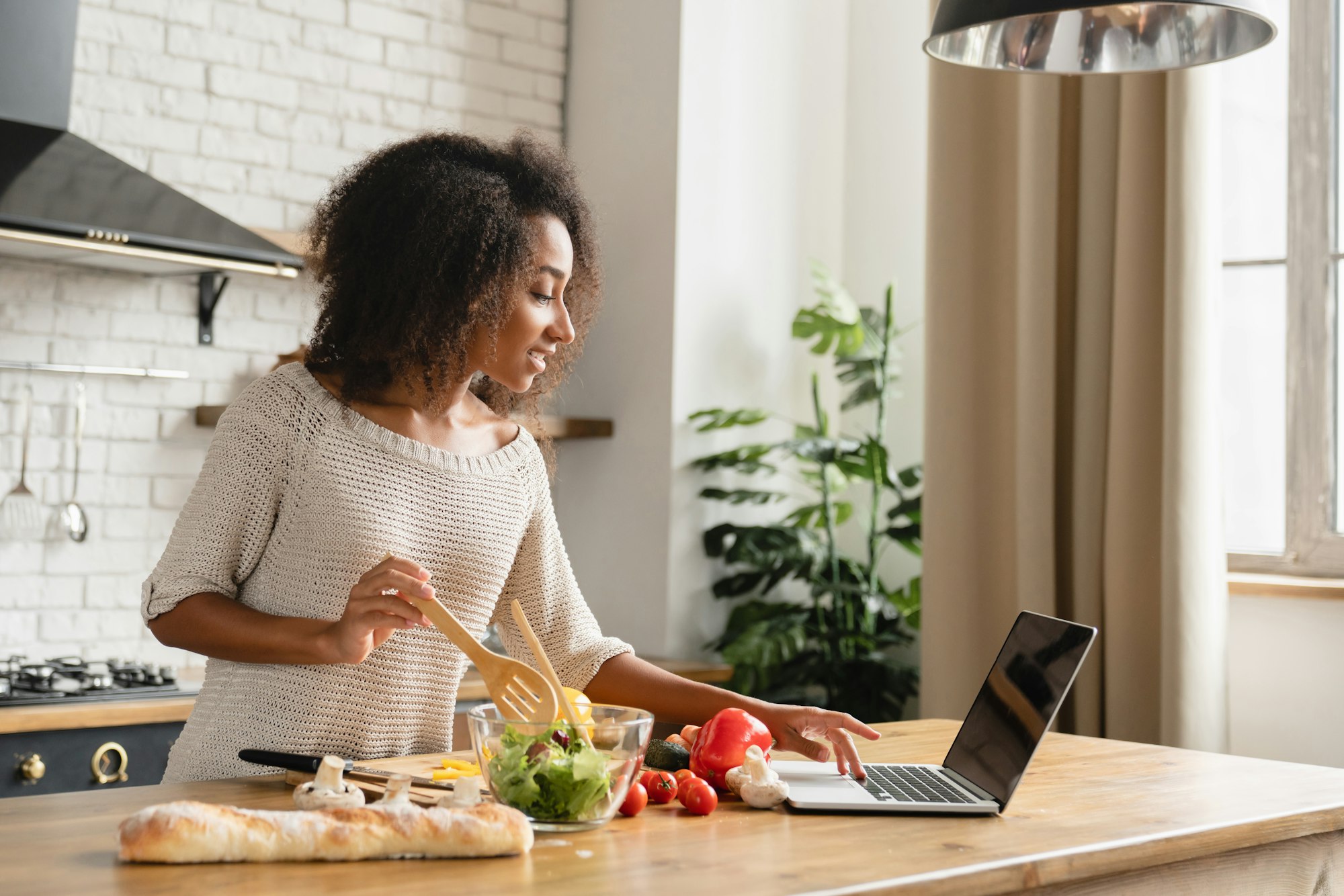 Girl using laptop for vlogging blogging looking for recipe while cooking vegetable vegan salad meal