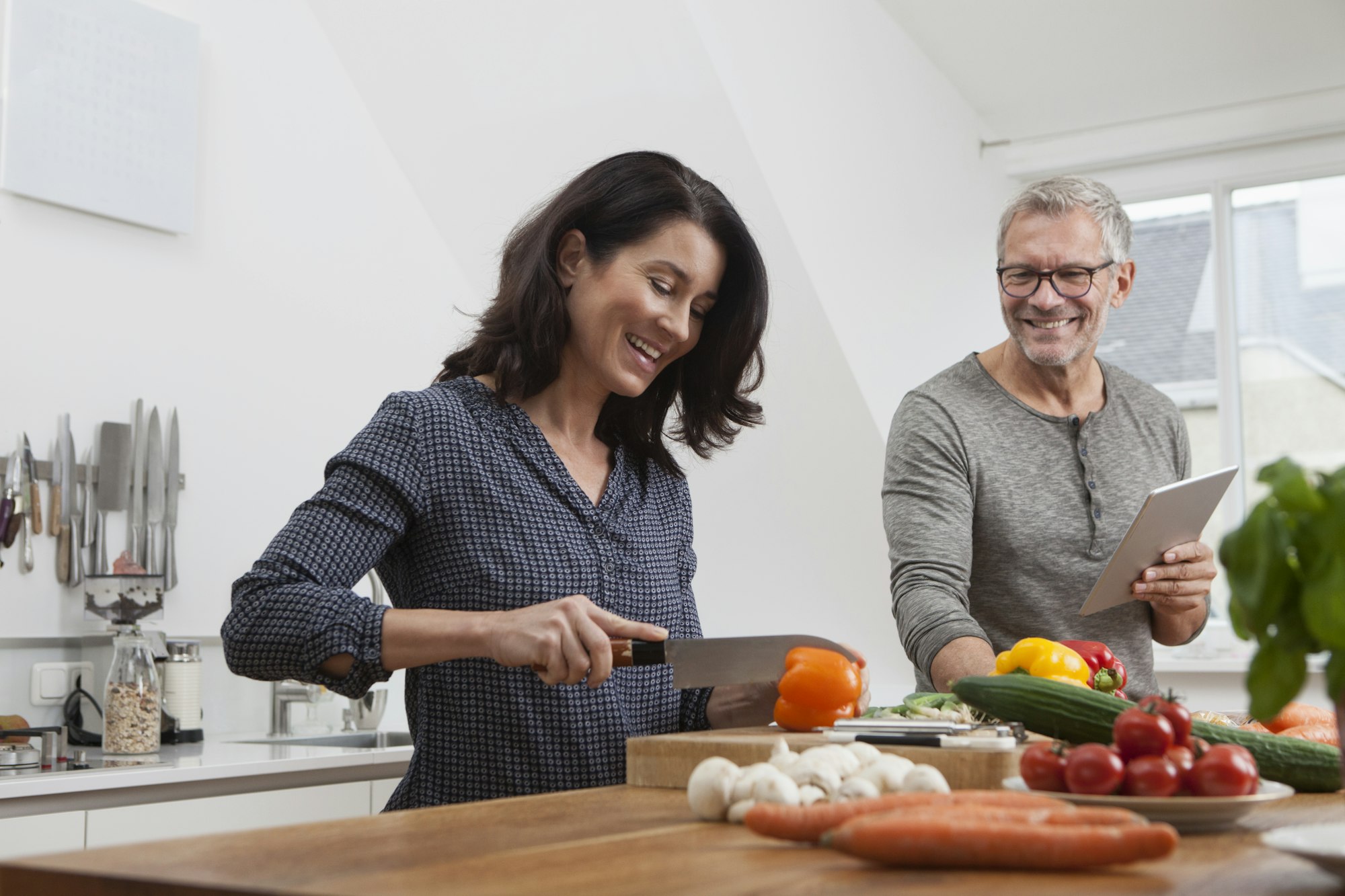 Mature couple with digital tablet cooking in kitchen